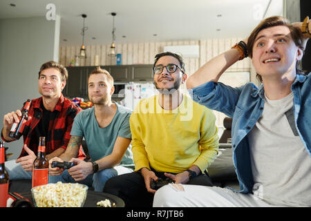 Emozionato simpatici amici radunati insieme a casa con birra e patatine e riproduzione di video giochi sulla TV Foto Stock