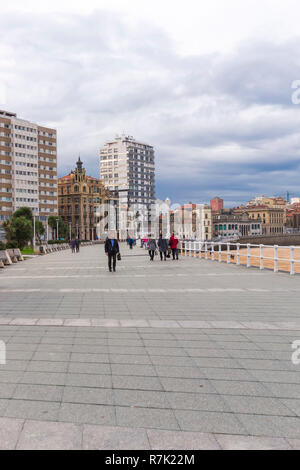 Una vista della spiaggia di San Lorenzo promenade a Gijon asturie spagna nel tardo autunno (caduta) con un cast di sky e la gente camminare sulla spiaggia sabbiosa. Foto Stock