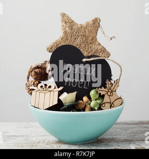 Primo piano di alcuni diversi accoglienti decorazioni di Natale in un blu Vassoio in ceramica e un cuore-forma cartello con il testo buon natale scritto in francese, Foto Stock