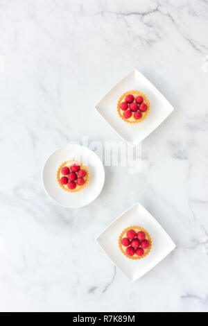 Pasticcini fatti in casa riempiti con lamponi freschi e crema di limone su porcellana bianca e piastre di marmo bianco. Vista dall'alto. Foto Stock