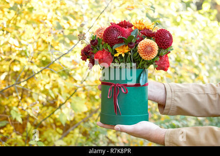 Bellissimo uomo in una tuta holding hands festosa scatola verde con fiori delicati.dono alla Giornata della donna. Close up vista laterale.Concetto per matrimoni, compleanni, e Foto Stock