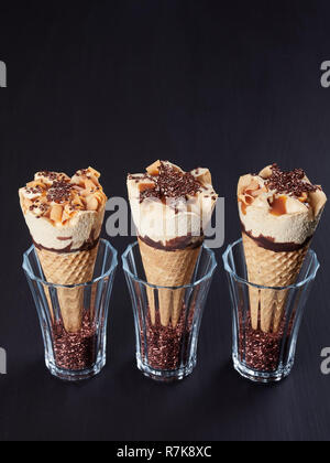 Tre caramello coni gelato, impostato in bicchieri riempiti con cristalli di zucchero, su scuro dello sfondo marrone Foto Stock