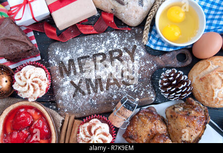 Merry Xmas scritto in farina su di un tagliere circondato da ingredienti di natale Foto Stock