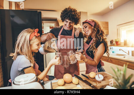 Felice famiglia giovane è la preparazione di pasto sano in cucina. Il padre è un cocktail di colata in vaso e madre e figlia stanno tenendo i vasetti per bere smo Foto Stock