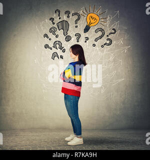 Vista laterale a piena lunghezza Ritratto di pensieroso giovane donna con le braccia incrociate. Riflessivo casual ragazza emozione meditativa segni di interrogazione, lampadina ed arro Foto Stock