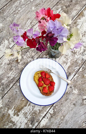 Regno Unito. In estate la colazione fuori in giardino - un piatto di fragole su toast alla francese, con un vaso di appena raccolte di piselli dolci su un vecchio tavolo in legno Foto Stock