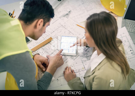 Vista superiore del successo di giovani architetti controllare i piani architettonici su tablet in ufficio. Foto Stock