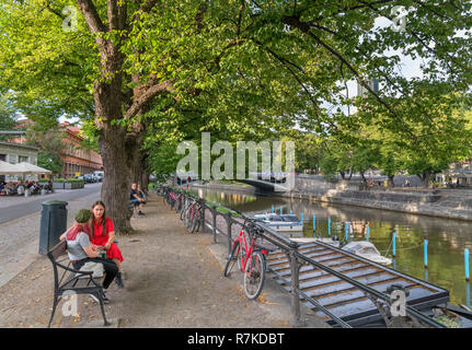 Due giovani donne seduti sulle rive del fiume Aura (Aurajoki) nel centro storico, Turku, Finlandia Foto Stock