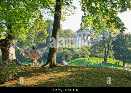 Le persone che si godono il sole autunnale nel Giardino Inglese, Monaco di Baviera. Il parco è un luogo popolare per rilassarsi su una bella giornata calda. Foto Stock