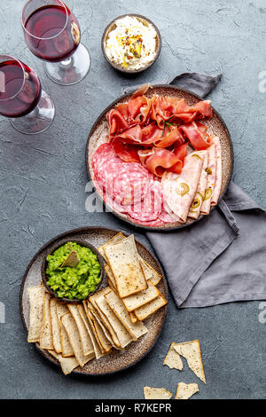 Antipasto. Piatto a base di carne, patatine e salse, vino rosso su sfondo grigio. Vista superiore Foto Stock