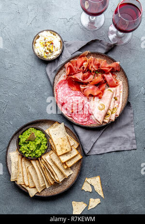 Antipasto. Piatto a base di carne, patatine e salse, vino rosso su sfondo grigio. Vista superiore Foto Stock