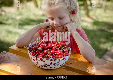 Adorabile ragazza bionda con frutti di ciliegio in mani Foto Stock