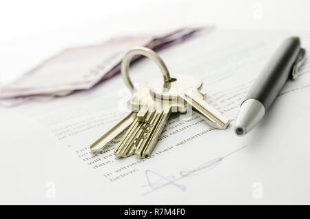 Le chiavi di una nuova casa su un contratto firmato della casa di vendita con i soldi in background. Concetto di chiusura della trattativa. Foto Stock