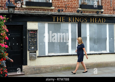 Una donna che cammina past​ un intavolato public house. Pub. Foto Stock