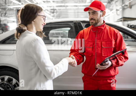 Giovane donna client stringono le mani con auto meccanico in rosso uniforme avente una trattativa in corrispondenza del servizio auto al seguito Foto Stock