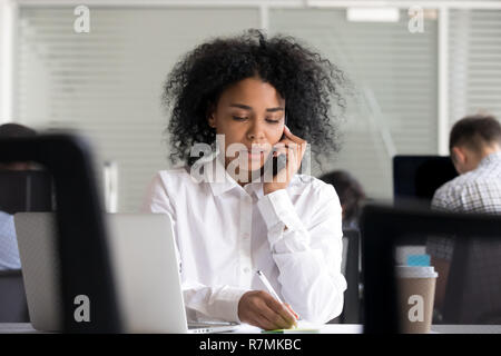 Focalizzato americano africano donna rendendo note, parlando al telefono Foto Stock