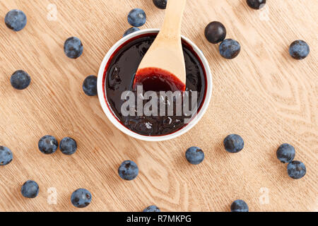 La composizione degli organici dolci sloe inceppamento in una ciotola con un cucchiaio di legno su un sfondo di legno. Vista superiore Foto Stock