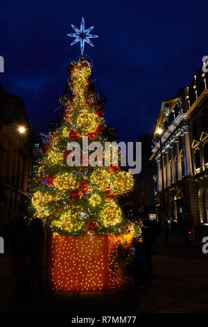 Le luci di Natale, con una stella sopra di loro, appendere su un albero di natale in St James Regent Street, Londra, 2018 come due bambini di sostare al di sotto di esse. Foto Stock