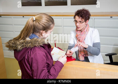 La pratica medica, la receptionist consegna un rinvio a un medico e una prescrizione per il paziente, presso la reception Foto Stock