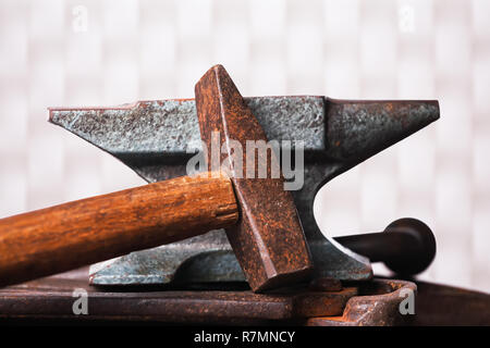 Vecchio arrugginito incudine robusto con martello bianco su sfondo a scacchi. Foto Stock