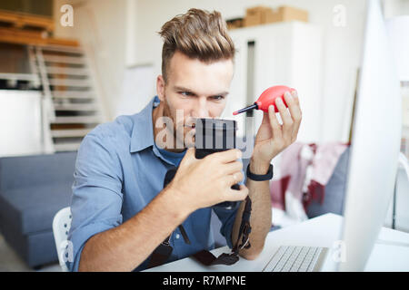 Ritratto di bel giovane foto di pulizia lente della fotocamera seduto alla scrivania , spazio di copia Foto Stock