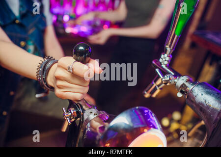 Giovane donna erogazione birra nel bar dalle imboccature di metallo. Bella barista toccando la birra nel bar. Foto Stock