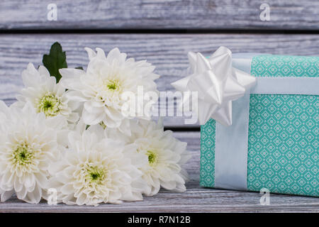 Close up bouquet di fiori e confezione regalo. Bella confezione regalo con bianchi crisantemi su sfondo di legno. Felice Festa della mamma. Foto Stock