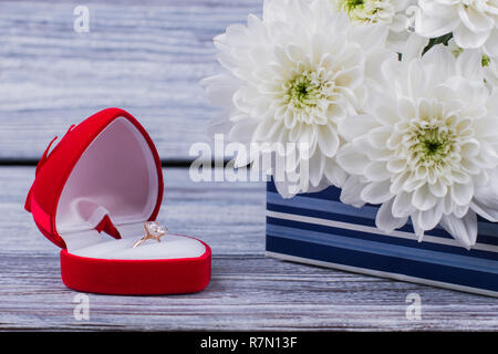 Anello di fidanzamento in una confezione regalo e bouquet di fiori. Close up red open box regalo con corona diamantata e la fioritura crisantemo fiori. Foto Stock