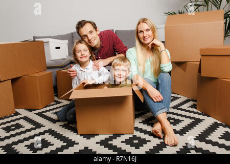 Immagine della giovane coppia con bambini seduti sul pavimento tra scatole di cartone nel nuovo appartamento Foto Stock