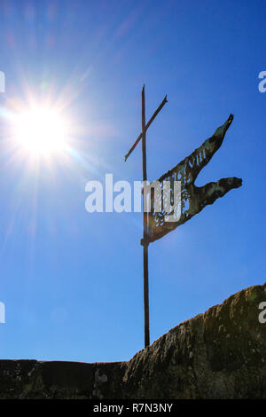 Bandiera di metallo sulla parte superiore della Fortezza di Montalcino la torre contro il cielo blu con sunburst, Val d'Orcia, Toscana, Italia. La fortezza fu costruita nel 1361 in cima th Foto Stock