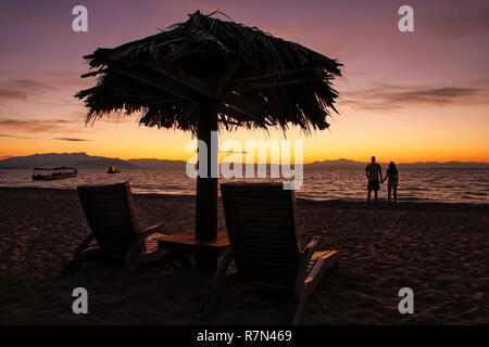 Stagliano lettini con ombrellone in paglia su una spiaggia di sunrise, South Sea Island, gruppo di isole di Mamanuca, Fiji. Foto Stock