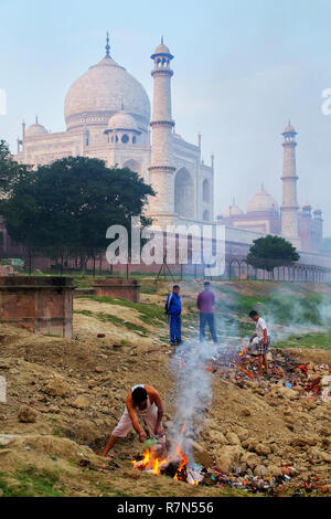 Gli uomini locali burning garbage sulla banca del fiume Yamuna vicino al Taj Mahal, Agra, Uttar Pradesh, India. Taj Mahal è stato designato come un patrimonio mondiale UNESCO Foto Stock