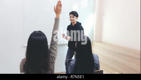 Gli studenti gruppo di alzare la mano per chiedere ad un amico Domande per insegnare a lavagna in aula Foto Stock