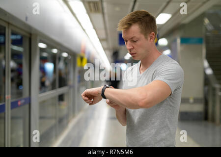 Giovane turista uomo tempo di controllo presso la stazione metro di Bangkok Foto Stock