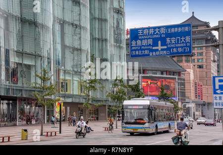 Wangfujing Street city center shopping con persone, bus, auto, scooters. l uomo Bicicletta Equitazione, Pechino, Cina Foto Stock