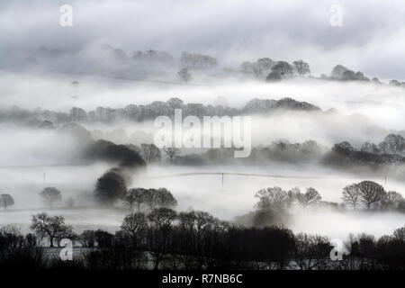 Guardando verso il basso sulla coperta di neve inglese farmland. Con alberi e siepi stagliano su un freddo, inverni, nebbioso giorno. Foto Stock