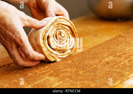 Close-up di chef le mani, che la laminazione di un rotolo di pasta con cannella per la torta. Messa a fuoco poco profonde. Foto Stock