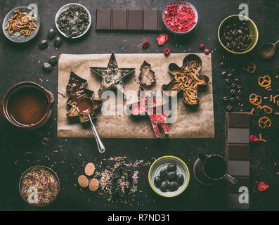 In casa natale di barre di cioccolato. Frese di natale con vari condimenti e aromi. Il cioccolato fuso nella ciotola con il cucchiaio sul rustico scuro k Foto Stock