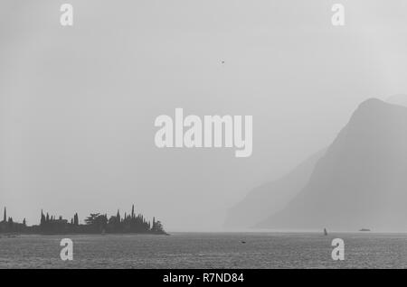 In bianco e nero vista sul mare di Garda con distand montagne e un parapendio nel cielo Foto Stock