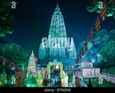 Una lunga esposizione dell'illuminato tempio di Mahabodhi a Bodh Gaya, con persone che si muovono dentro e fuori, e un po' di bandiere sventolano al vento, contro un cielo scuro Foto Stock