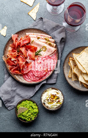 Antipasto. Piatto a base di carne, patatine e salse, vino rosso su sfondo grigio. Vista superiore Foto Stock