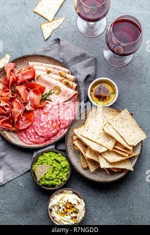 Antipasto. Piatto a base di carne, patatine e salse, vino rosso su sfondo grigio. Vista superiore Foto Stock