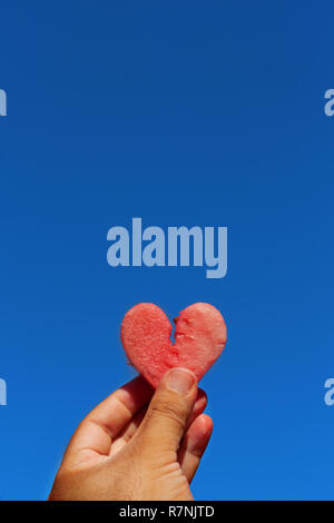 Uomo con fetta di anguria a forma di cuore contro il cielo blu. Fetta di cocomero contro il luminoso cielo estivo. Spazio di copia Foto Stock