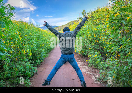 L'uomo solo rilassante su una strada rurale con due lati della strada è selvaggio girasoli fioriscono in giallo e colorati di scena, bellissima natura Foto Stock