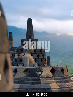 Un Buddha statua di pietra sanciti in una forma di campana stupa domina la vallata sulla sommità del tempio buddista di Tempio di Borobudur, una attrazione turistica nel centro Foto Stock