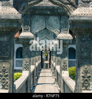 I turisti vengono visualizzati nell'perspetive del ponte ad arcate e centrale padiglione flottante di Taman Ujung Royal Palace e giardino, Bali, Indonesia. Foto Stock