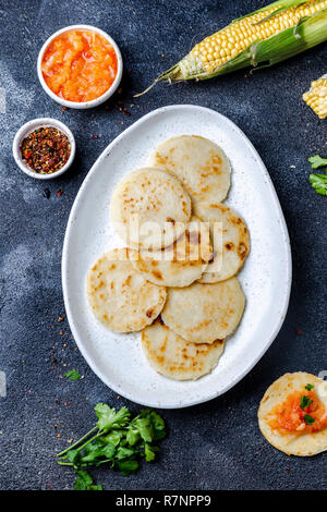 Cibo colombiano. AREPAS di mais e di maiale fritto chicharron ans colombiano di salsa di pomodoro. Vista dall'alto. Sfondo nero Foto Stock