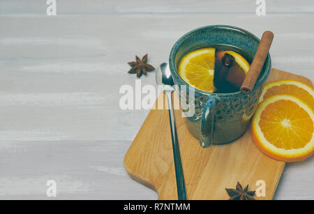 Una tazza di ceramica di riscaldamento tè con cannella e arancio su un rustico tavolo bianco. copia spazio. vista verticale .. Foto Stock