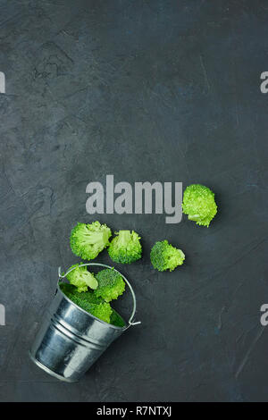 Placer broccoli verdi segmenti da un piccolo cucchiaio. Mangiare sano pattern su sfondo scuro. Spazio Copia vista dall'alto. Cibo vegetariano. Foto Stock