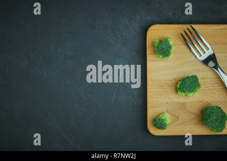 Placer broccoli verdi segmenti da un piccolo cucchiaio. Mangiare sano pattern su sfondo scuro. Spazio Copia vista dall'alto. Cibo vegetariano. Foto Stock